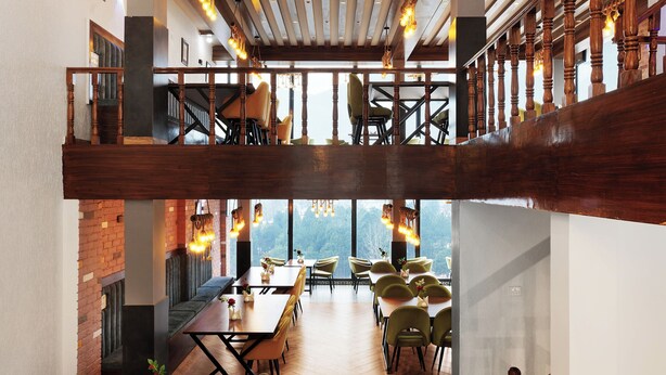 Une vaste salle à manger dotée d’un haut plafond, de poutres en bois et d’un lustre. Un escalier y mène à un niveau supérieur.