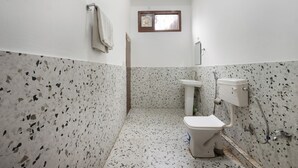 Une salle de bain avec des toilettes blanches, un lavabo sur colonne et une douche. Les murs sont recouverts de carreaux à motifs pointillés.