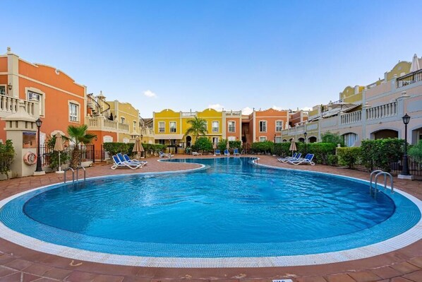 Una gran piscina al aire libre rodeada de edificios coloridos, con sillas de descanso y sombrillas.