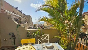 Un coin repas avec une table dressée pour deux personnes, des chaises d’extérieur et une vue sur le paysage urbain.