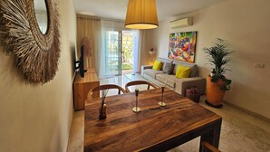 Un salon moderne avec une table à manger en bois, un canapé agrémenté de coussins jaunes, un grand miroir et un tableau coloré accroché au mur.
