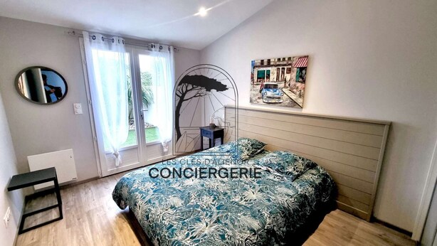 Un dormitorio con cama, ventana con cortinas, espejo en la pared y un cuadro.