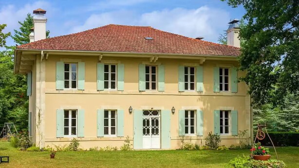 Ein zweistöckiges Gebäude mit symmetrischer Fassade, einem zentralen Eingang mit einer verzierten Tür und einem roten Ziegeldach.