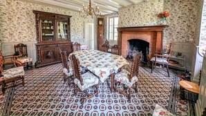 Ein Esszimmer mit einem großen Tisch, verzierten Stühlen, einem Kamin und Wandpapier mit Muster.