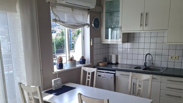 A modern kitchen with white cabinets, a built-in dishwasher, and a dining area with a white table and chairs. - Mogan Playa 19 by El Sirocco (Mogan)