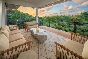 A balcony with wicker furniture, a stone table, and a view of lush greenery and distant buildings.