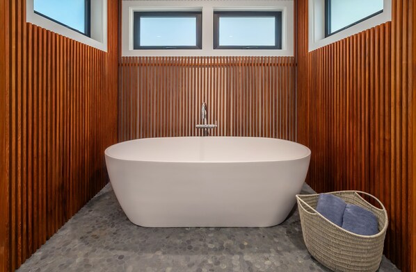 A modern bathroom with a freestanding bathtub, wooden paneling, and a small wicker basket.