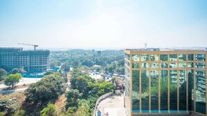 Un edificio de gran altura con fachada de vidrio moderna, rodeado de vegetación y otros edificios.