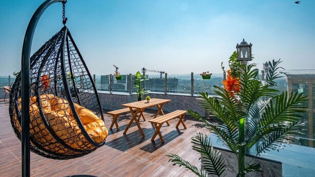 Una terraza en la azotea con una silla colgante, mesas de madera y plantas en macetas.