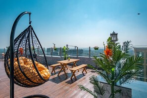 A rooftop terrace with a hanging chair, wooden tables, and potted plants. - Rooftop Suite 3 BHK ( Gagal Home) (Mumbai)