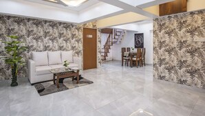 Un salón amplio con un sofá blanco, una mesa de centro y una mesa de comedor con sillas. Una escalera conduce a un nivel superior.