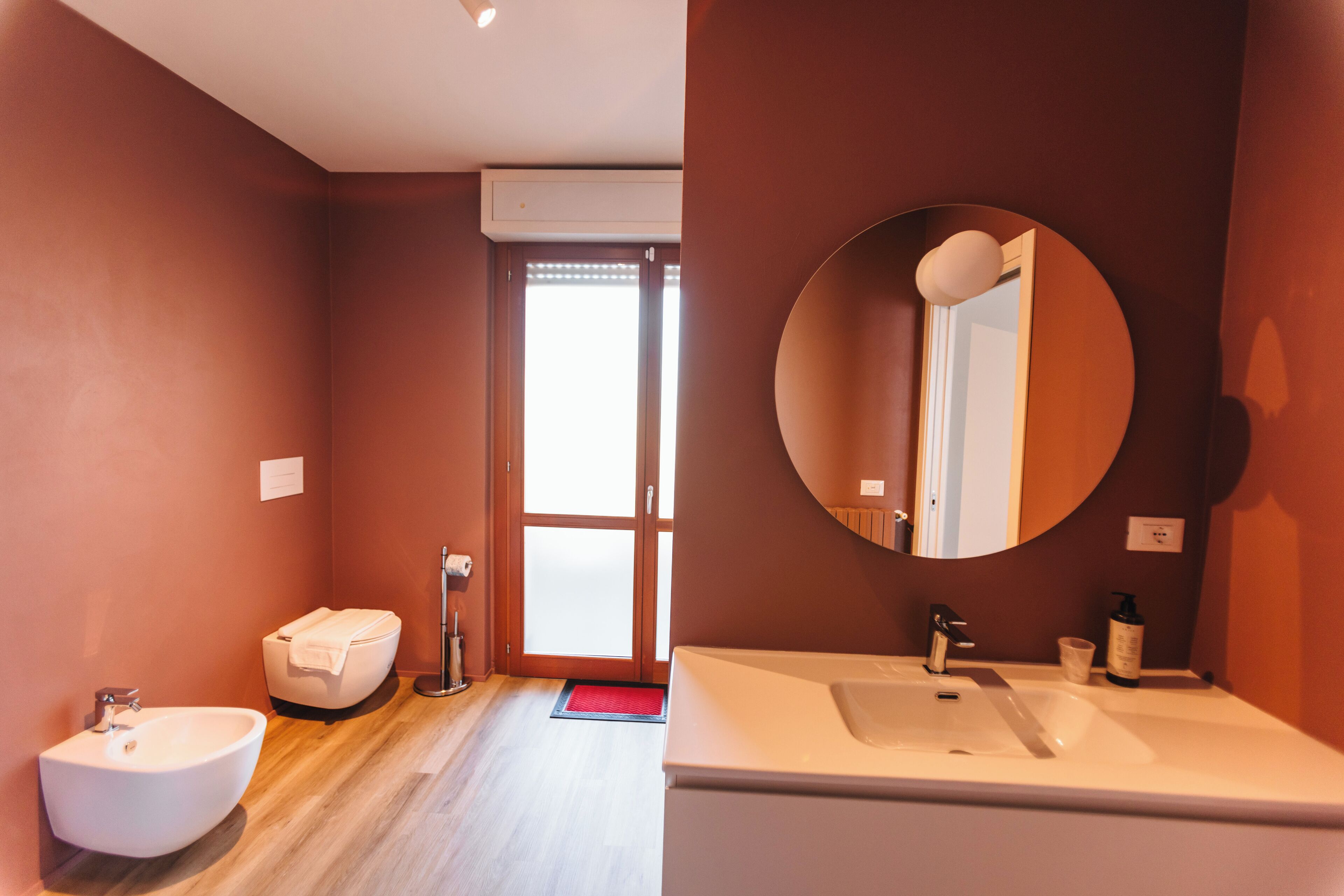 A modern bathroom with a large round mirror, a sink, a bidet, and a toilet.