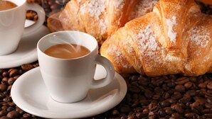 Two white cups of coffee on saucers, a croissant, and coffee beans. - La Culla dei Sogni (Pescara)