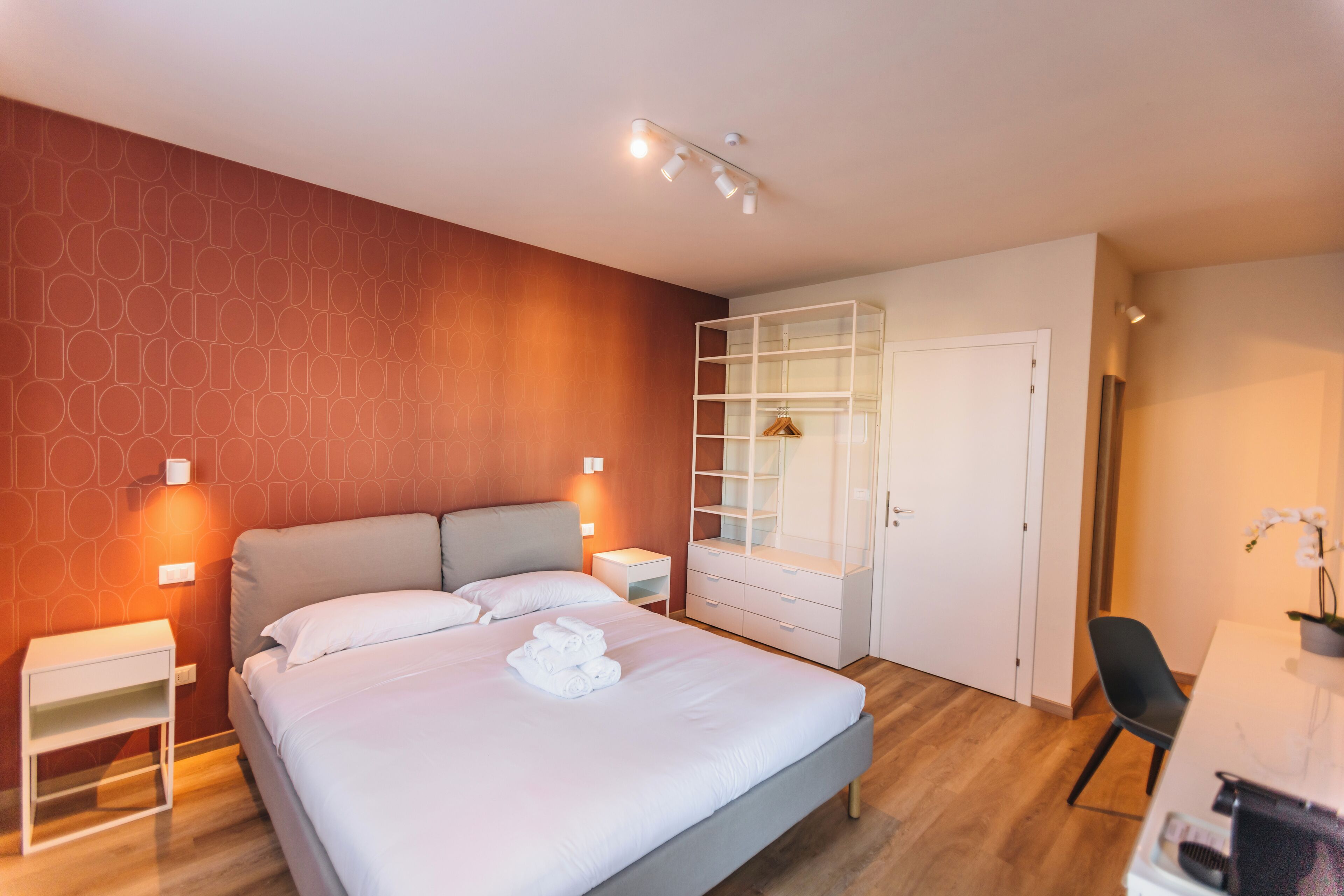 A modern hotel room with a large bed, a wardrobe, a desk, and a chair.