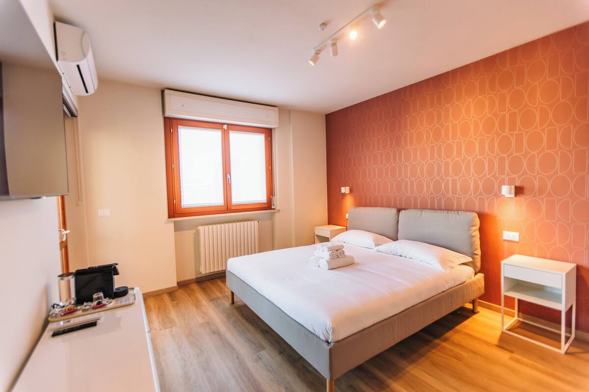 A modern bedroom with a large bed, bedside tables, a window, and a radiator.