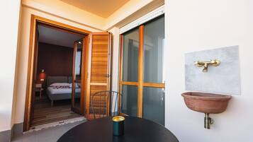 Een kamer met een bed, een stoel, een tafel met een kopje, een raam en een wastafel.