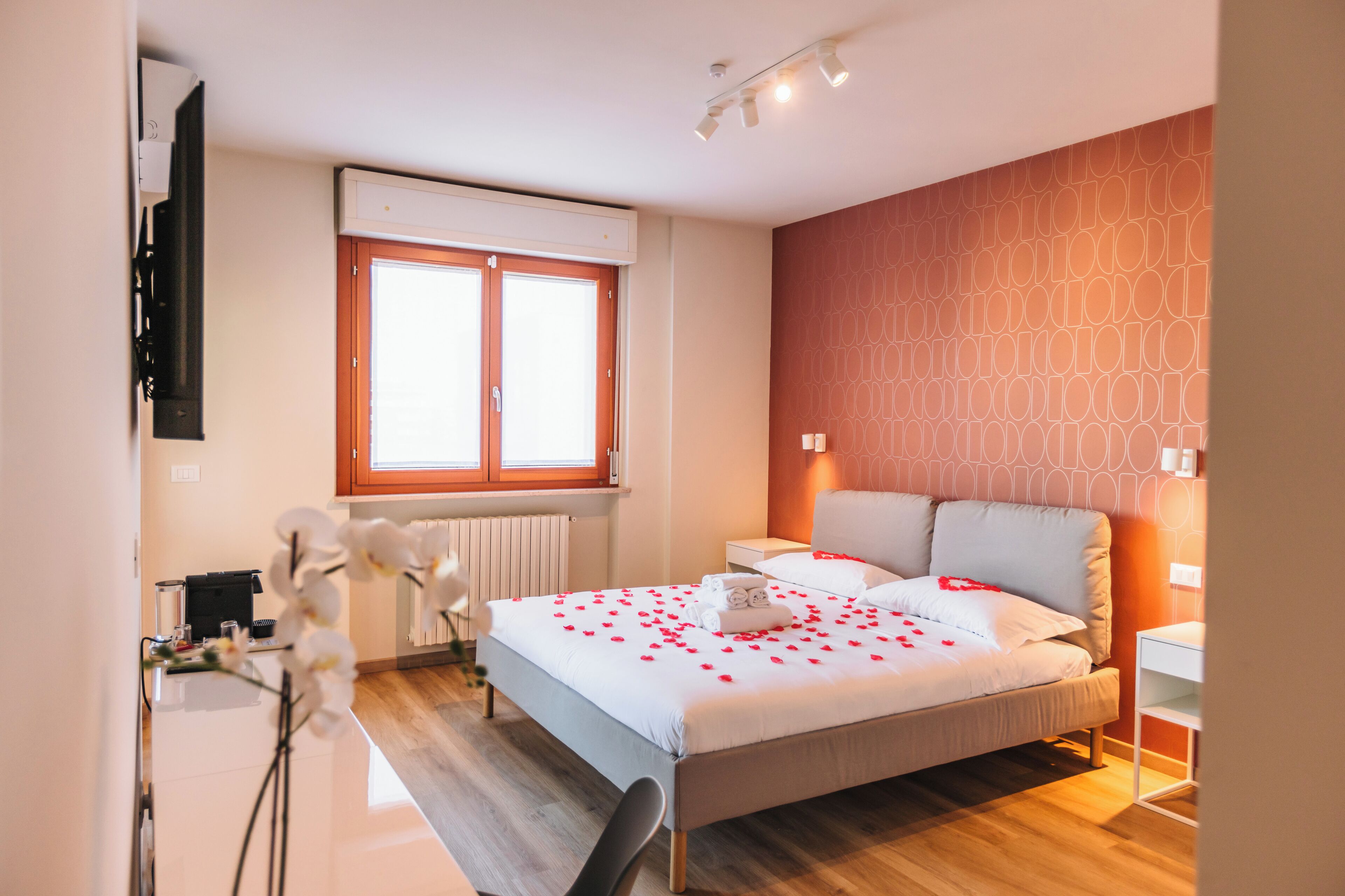A hotel room with a bed, bedside tables, a desk, a chair, and a window.