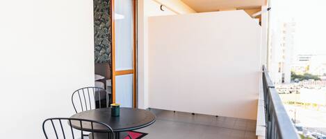 Un balcón con una mesa redonda y sillas, una puerta que da a una habitación y vistas de la ciudad.