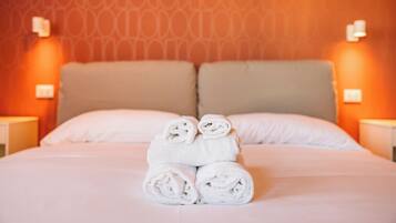 A neatly made bed with rolled white towels in the center, a patterned wall, and two bedside lamps.