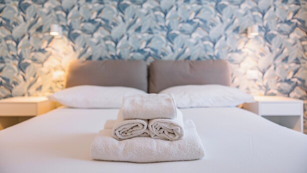A neatly made bed with folded towels and a patterned wall in the background. - La Culla dei Sogni (Pescara)