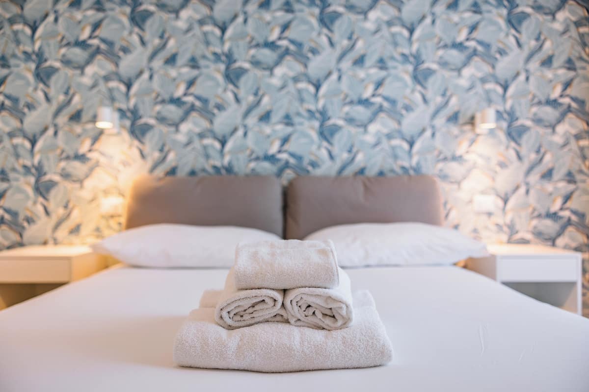A neatly made bed with folded towels and a patterned wall in the background.