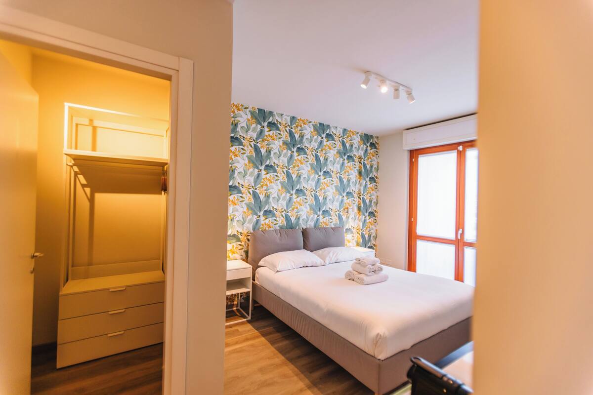 A bedroom with a bed, a bedside table, a wardrobe, and a window with curtains.