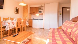 A cozy living room with a sofa and a wooden table, a dining area with chairs and a table, and a kitchen with wooden cabinets and a microwave. - Apartment for 6 in Aussois, balcony and wifi at reception (Aussois)