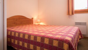 A bedroom with a wooden headboard, a checkered bedspread, a bedside lamp, and a window with curtains. - Apartment for 6 in Aussois, balcony and wifi at reception (Aussois)