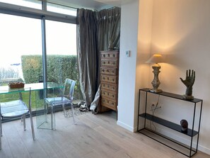 Ein modernes Zimmer mit einem Glastisch und Stühlen, einer Holzkassette mit Schubladen und einem Konsolentisch mit Lampe und Skulptur.