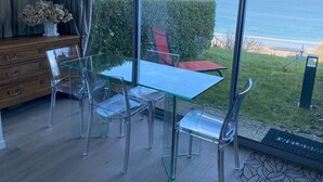 Ett modernt rum med ett glasbord och stolar, en byrå i trä och utsikt över havet.