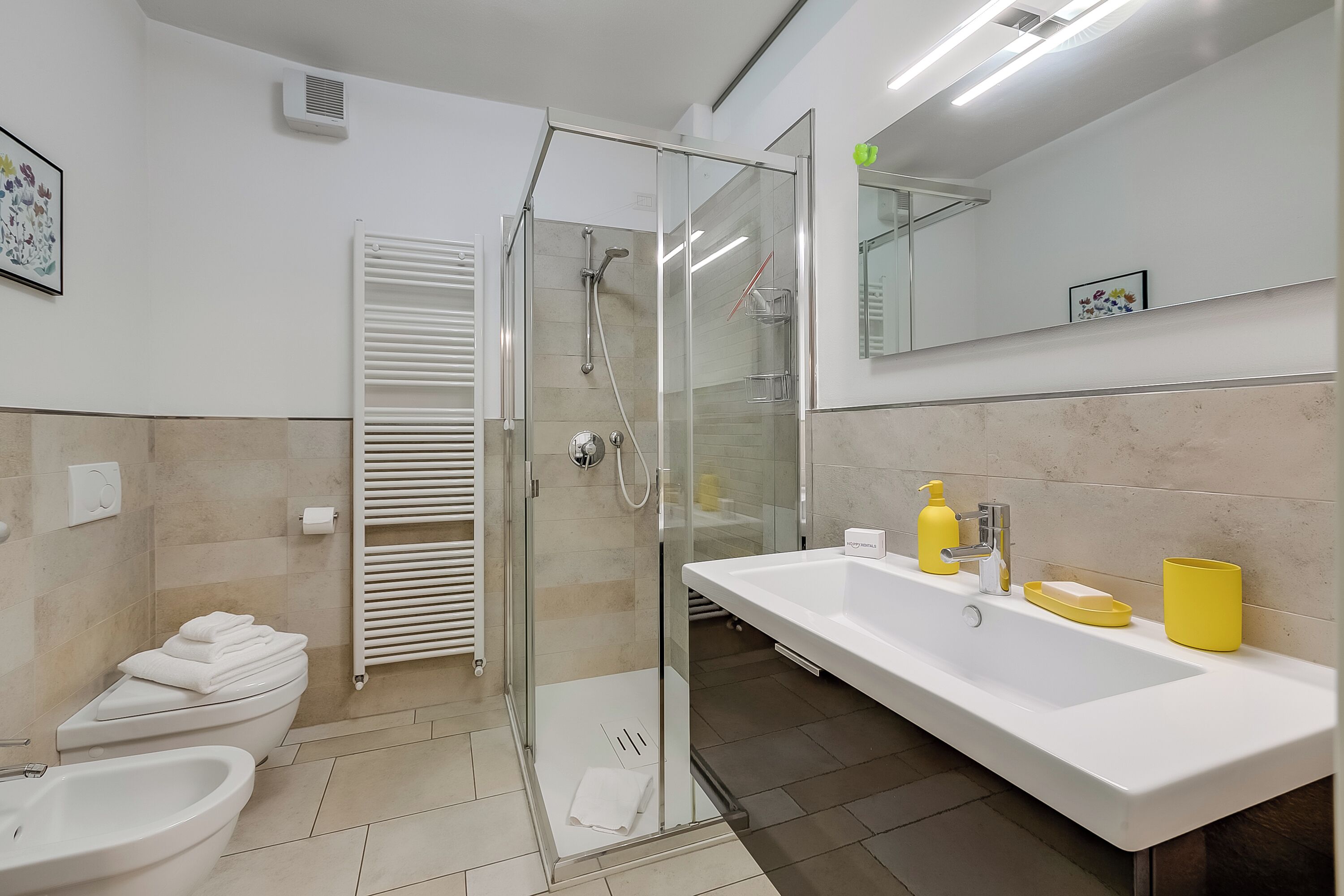 A modern bathroom with a glass-enclosed shower, a white sink with a yellow soap dispenser, and a white toilet.