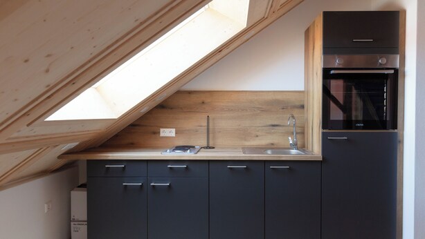 A compact kitchen with a skylight, built-in oven, and dark cabinetry.