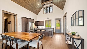 A spacious kitchen with a wooden dining table and chairs, a central island, and a high ceiling with exposed beams. - Camp Care Free at Eagles Nest - game room, hot tub, fire pit (Banner Elk)