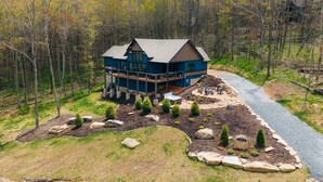 A large, two-story house with a deck, surrounded by a landscaped garden and a gravel path. - Camp Care Free at Eagles Nest - game room, hot tub, fire pit (Banner Elk)