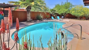 Una piscina con cubierta de madera, rodeada de cactus y una palmera.