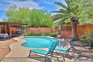 A swimming pool with lounge chairs, a covered patio, and a brick wall.