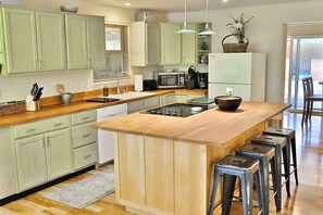 A modern kitchen with green cabinets, a wooden countertop, a central island with stools, and a refrigerator.