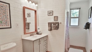 Un baño con pared de ladrillo blanco, un lavabo con espejo, inodoro y zona de ducha.