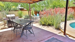 Un patio exterior con mesa y sillas, una parrilla y una piscina.