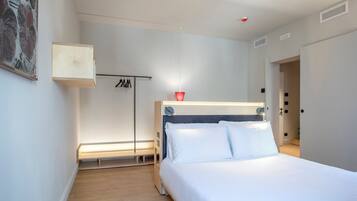 A modern bedroom with a wooden floor, a bed with white linens, a bedside table, a hanging light, and a coat rack.