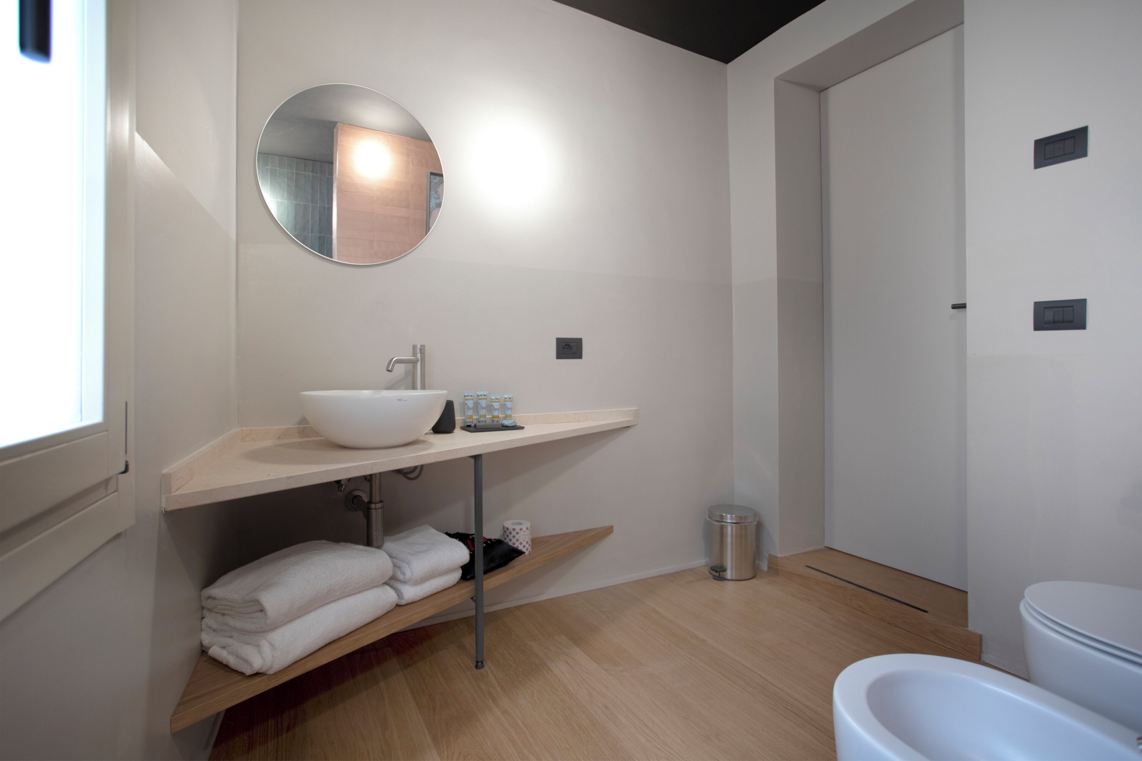 A modern bathroom with a white sink, mirror, and toilet. There is a towel rack and a trash can.