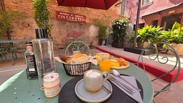 An outdoor dining area with a table set for breakfast, including croissants, a coffee cup, and a glass of orange juice.