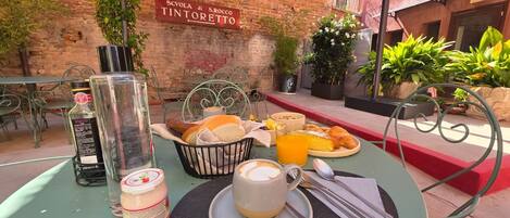 An outdoor dining area with a table set for breakfast, including croissants, a coffee cup, and a glass of orange juice.