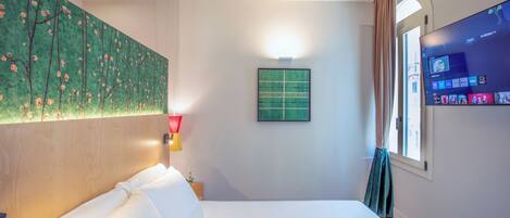 A hotel room with a bed, a painting on the wall, a TV, and a window with curtains.