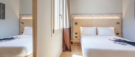 Una habitación de hotel con dos camas, suelo de madera y un amplio ventanal con cortinas.