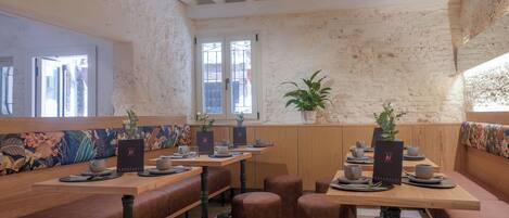 A restaurant with wooden tables and benches, a brick wall, and a window with a view.