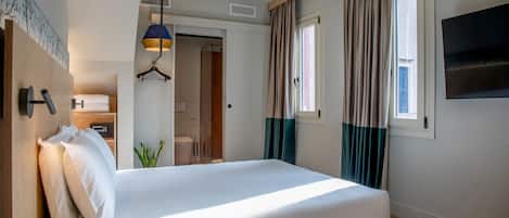 Een hotelkamer met een bed, een kledingkast, een hanglamp, een raam met gordijnen en een televisie aan de muur.