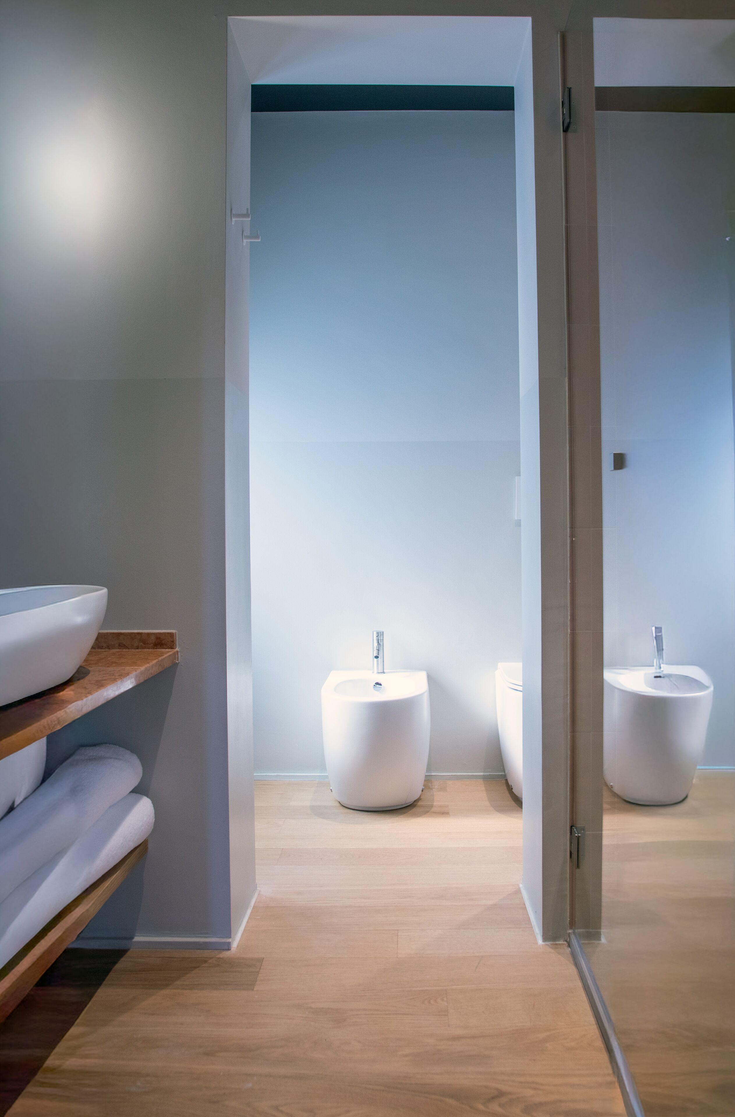 Un bagno moderno con un mobile contenitore in legno, due lavabi a colonna bianchi e uno specchio.