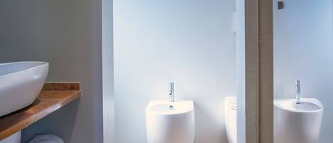 A modern bathroom with a wooden vanity, two white pedestal sinks, and a mirror.