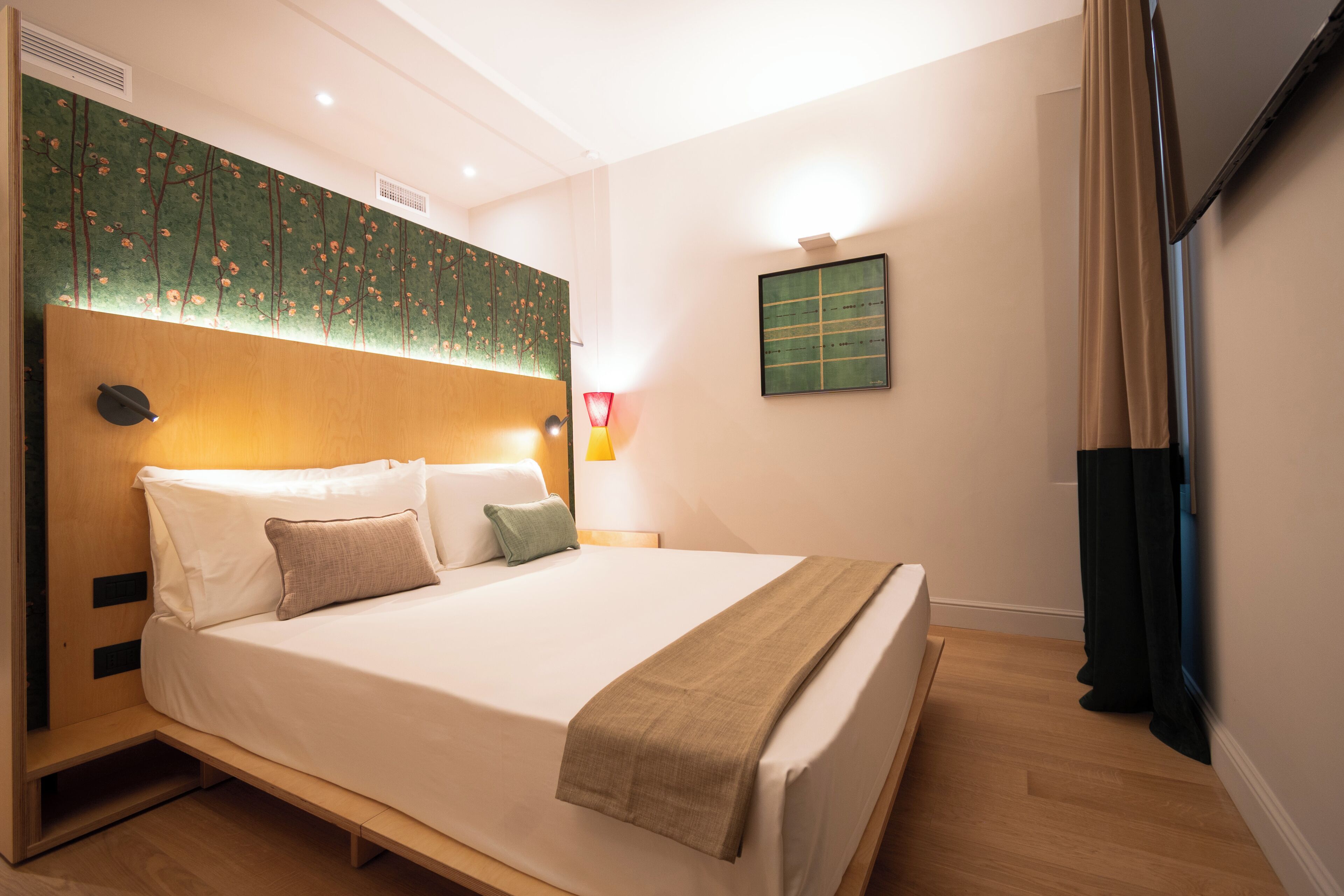 A neatly made bed with a headboard, a bedside table with a lamp, and a wall-mounted artwork.